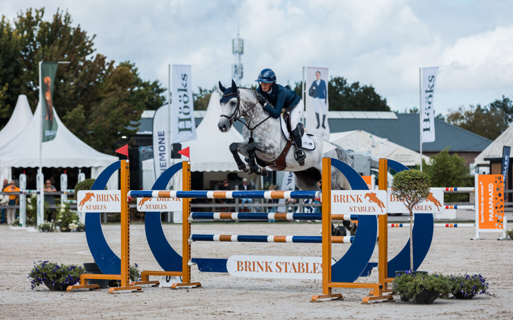Ruiter springt over een blauwe hindernis bij Brink Stables